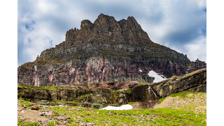 dramatic jagged mountain peak of Mt Reynolds and verdant summer landscape in Logan Pass in the Glacier National Park in Montana.