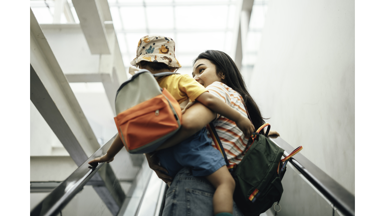 Mother And son  carrying rucksack while riding an escalator, commuting to school