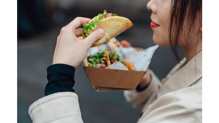 Young woman taking lunch break and enjoying tacos in street food market