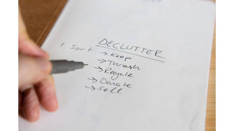 A person taking declutter notes on a paper (list; keep, recycle, thrash, donate, sell)