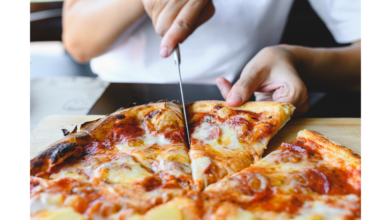 Wood fire cheesy pizza slice in hand. Traditional Hawaiian and Salami pizza savory dish flavour of origin Italian restaurant. Wood-Fired Oven Pizza with people holding and cutting knife background