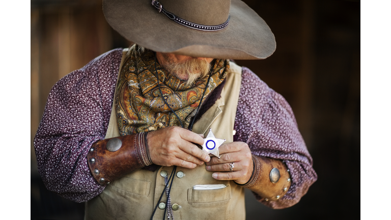 Senior male cowboy wearing star shaped badge at stable