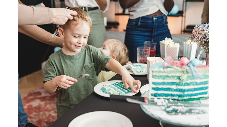 Two Happy Young Caucasian Boys Enjoying A Birthday Party And Eating Delicious Blue Cake