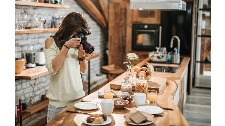 Female photographer taking photos of food at dining table.