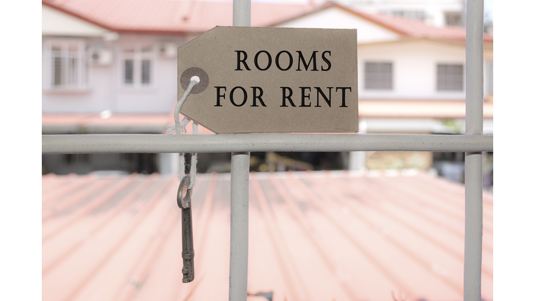 Text on brown paper and key hanging on the window grill with blurred background of houses - Rooms for rent