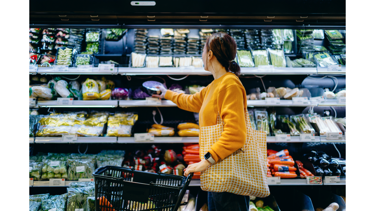 Young Asian woman with shopping cart, carrying a reusable shopping bag, shopping for fresh organic fruits and vegetables in supermarket. Environmentally friendly concept. Zero waste and plastic free. Eco friendly shopping. Sustainable living lifestyle