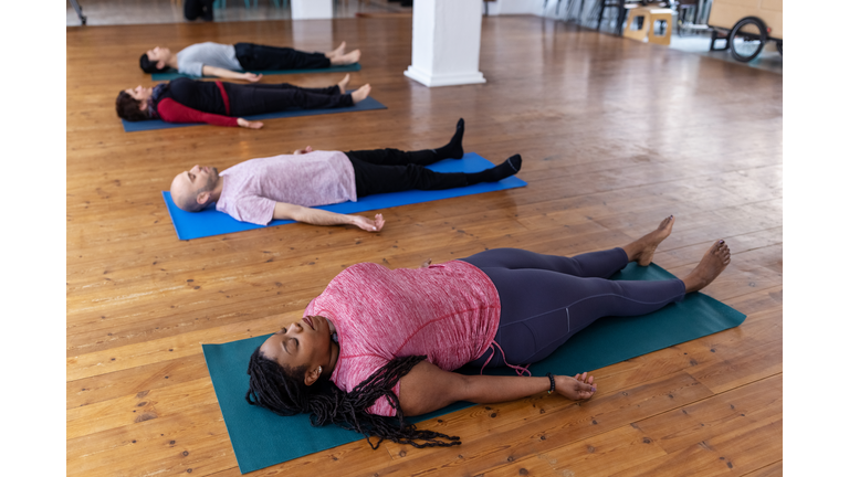 Multiracial people lying on exercise mat in yoga class