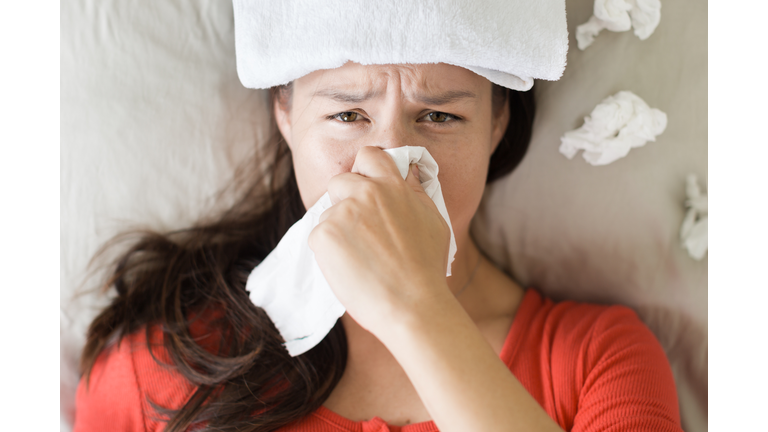 Sick woman coughing and blowing her nose, lying in bed.