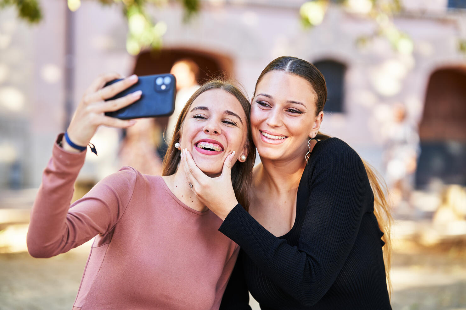 Two cheerful women smiling very affectionately looking at a phone while taking a selfie, front view