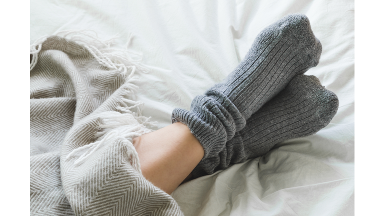 Feet crossed with gray socks on bed under blanket