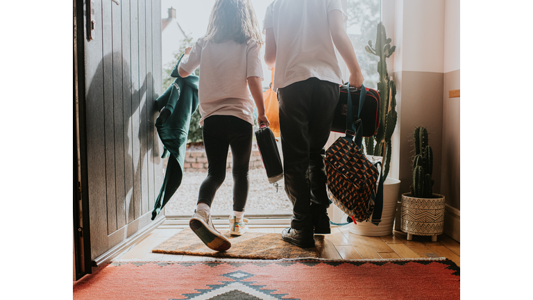 Two young children wearing school uniforms exit their front door