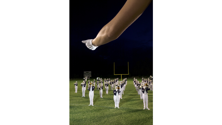 Close-up of the drum major's gloved hand directing the marching band in the background.