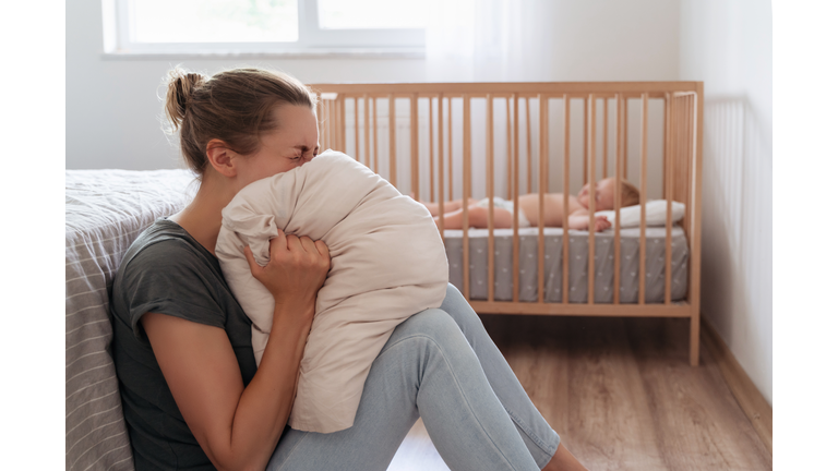 Depressed mother screaming with desperation in pillow to overcome negative emotions