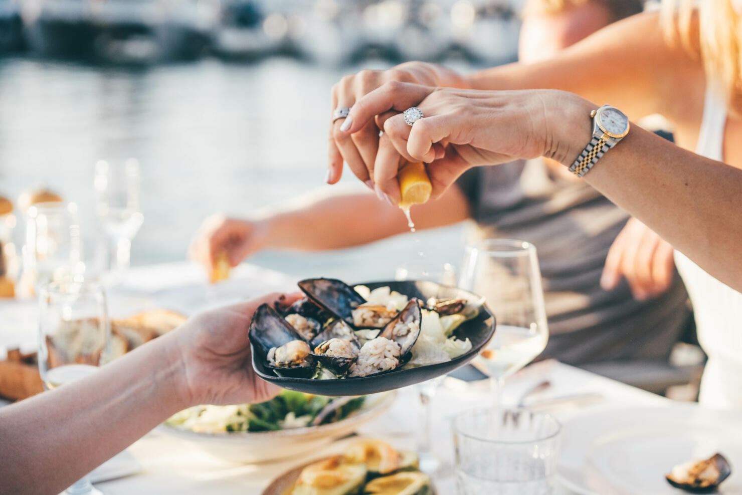 Close up of a woman's hand squeezing lemon juice on to mussels, enjoying meal in a restaurant.