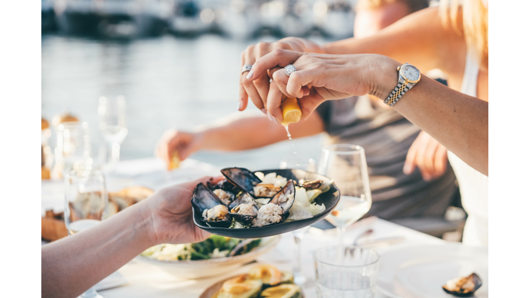 Close up of a woman's hand squeezing lemon juice on to mussels, enjoying meal in a restaurant.