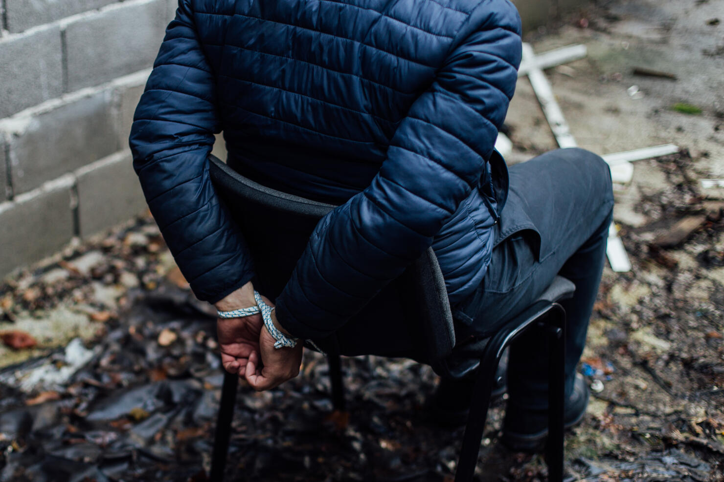 A man with his hands tied on his back sitting on a chair