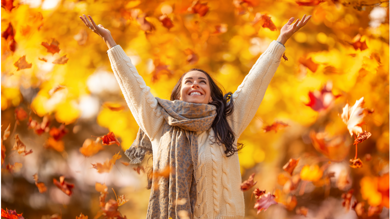 A happy young woman in a park throws leaves during an Indian summer and enjoys autumn.