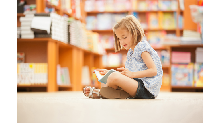 Girl sitting on floor of library with book