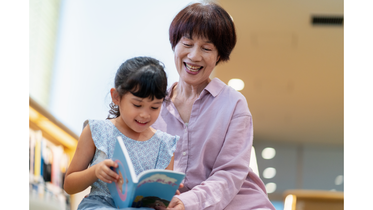 Senior woman teaching her granddaughter to read at the library