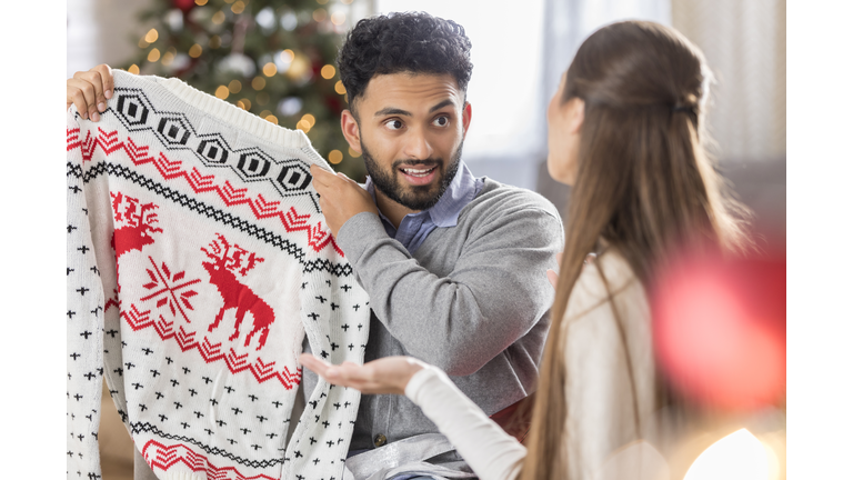 Man with funny expression holds up Christmas sweater