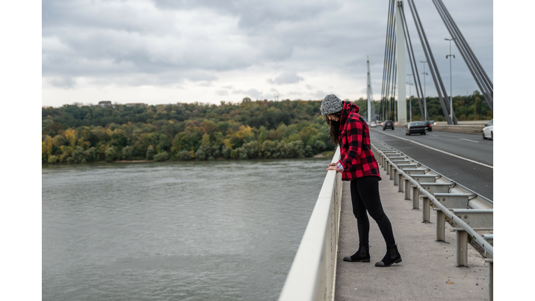 Young depressed homeless girl or woman standing alone on the bridge want to jump in to the water of the river and to commit suicide after hard life on the street selective focus