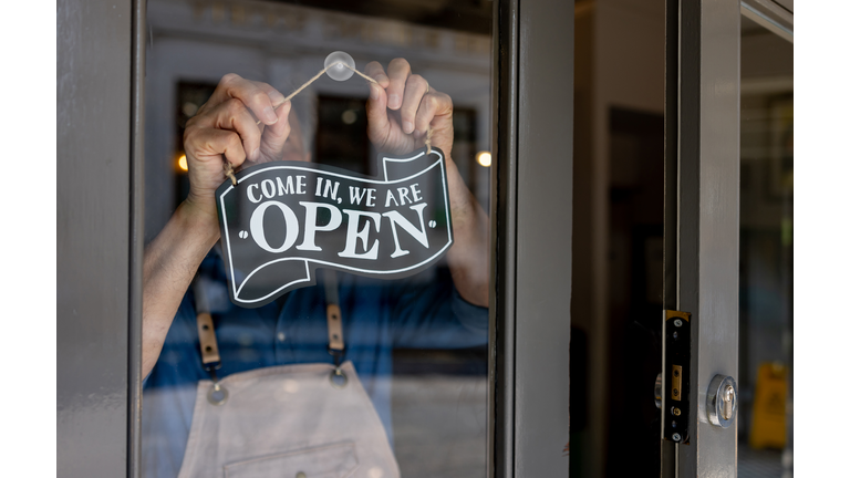 Close-up on a business owner hanging an open sign on the door of his restaurant