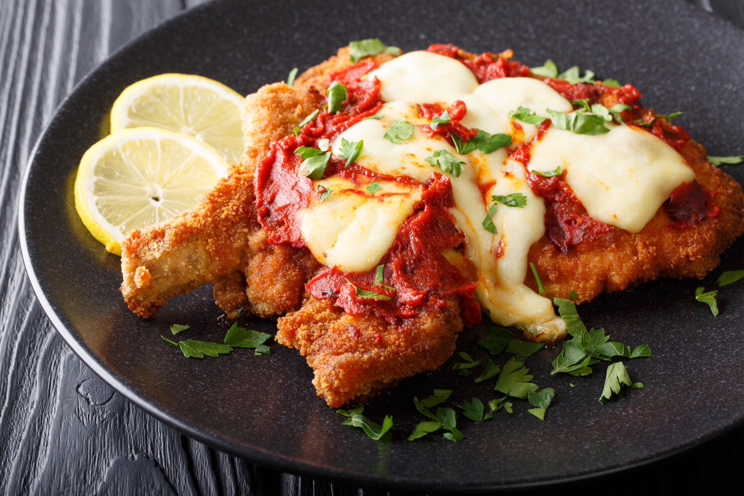 La milanesa napolitana - homemade veal cutlet with mozzarella cheese, lemon and tomato sauce close-up. Horizontal