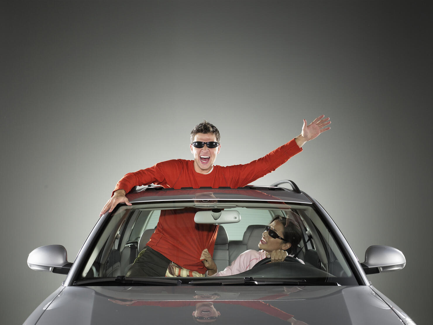Young man and woman in car, man hanging out sun roof, waving