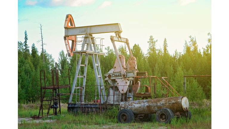 An abandoned oil or gas rocking machine against a blue sky, exhausted resource. Clogged field of gas and oil production.