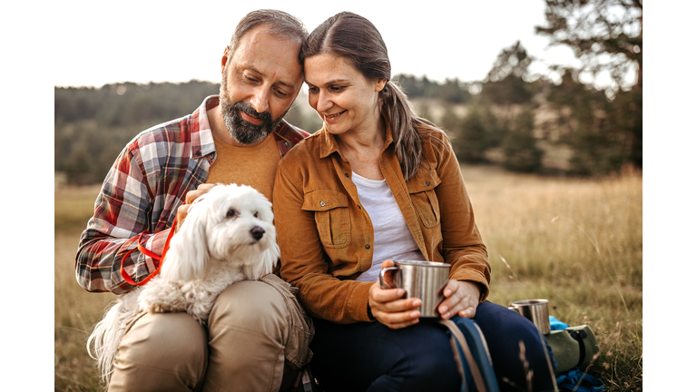 Couple with pet dog relaxing while hiking at forest