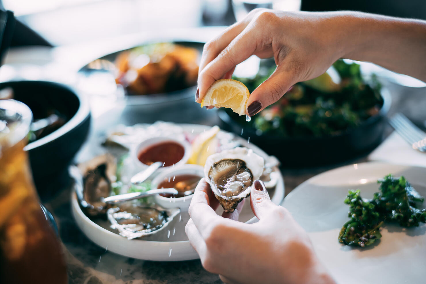 Close up of a woman's hand squeezing lemon juice on to a fresh oyster, enjoying a scrumptious meal in a restaurant. Eating out lifestyle