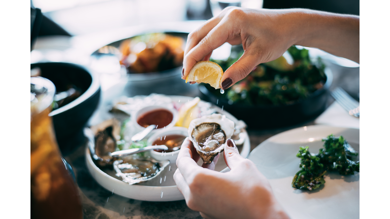 Close up of a woman's hand squeezing lemon juice on to a fresh oyster, enjoying a scrumptious meal in a restaurant. Eating out lifestyle