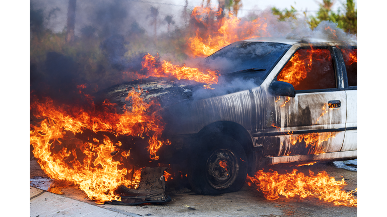 Close-up of burning car after a frontal crash collision on the roadside with flame and smoke.