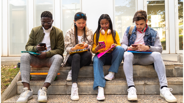 Group of multiracial teenage college friend students ignoring each other looking at mobile phone. Smartphone addiction.