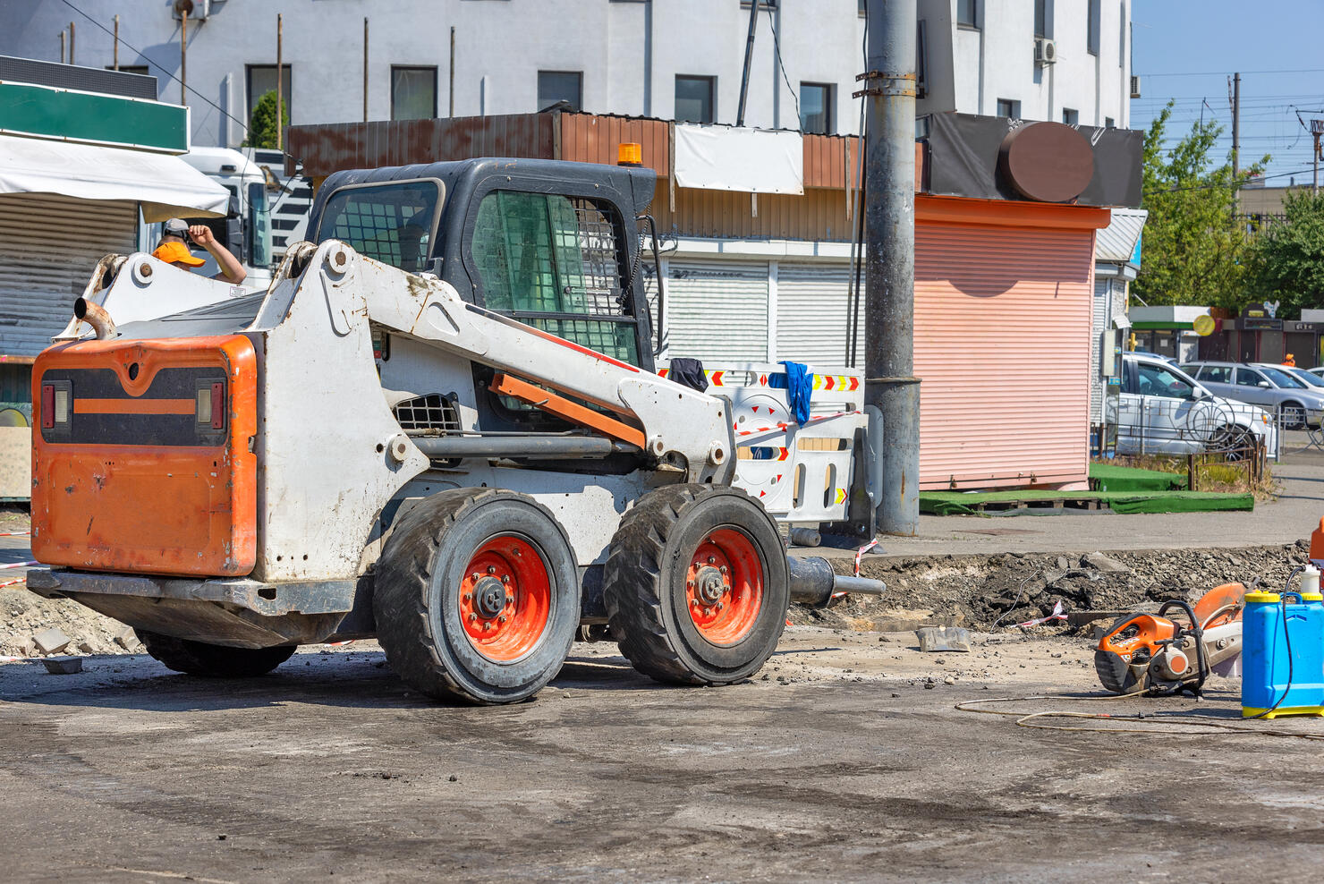 A highly manoeuvrable construction vehicle with a jackhammer attached is parked at a work site with a city street being repaired in the background.