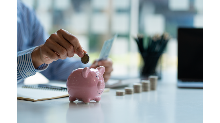 Hands of a young Asian businessman Man putting coins into piggy bank and holding money side by side to save expenses A savings plan that provides enough of his income for payments.