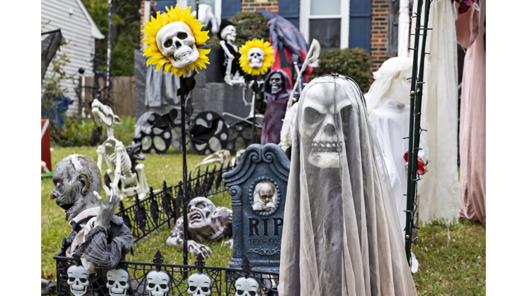 Creepy grim reaper sits in the front of a heavily decorated Halloween yard