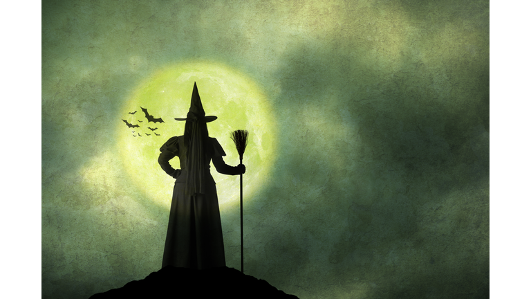 Halloween Witch Holds Her Broom Standing In Front Of Full Moon