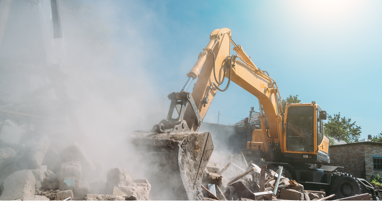 Destruction of old house by excavator. Bucket of excavator breaks concrete structure