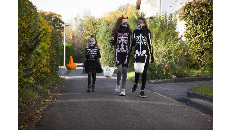 Child and teenagers walking along a narrow urban street whilst out trick or treating for Halloween