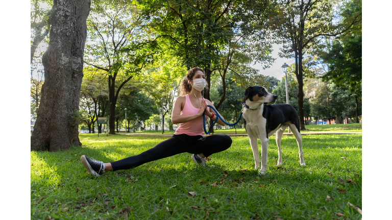 Woman doing tai chi at the park with her dog and wearing a facemask