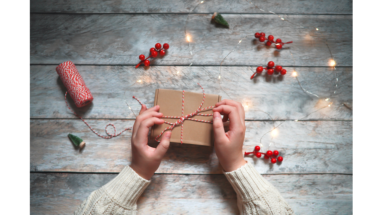 Hands close-up packing Christmas gift in brown box. Top view, wooden background