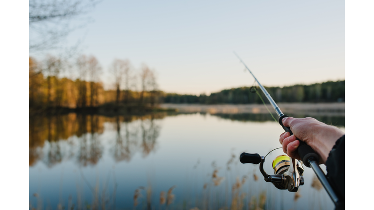 Fishing. Fisherman with rod, spinning reel on the river bank. Fishing for pike, perch, carp. Fog against the backdrop of lake. background Misty morning. wild nature. Article about fishing day.