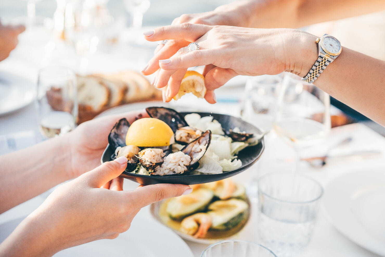 Close up of a woman's hand squeezing lemon juice on to mussels, enjoying meal in a restaurant.