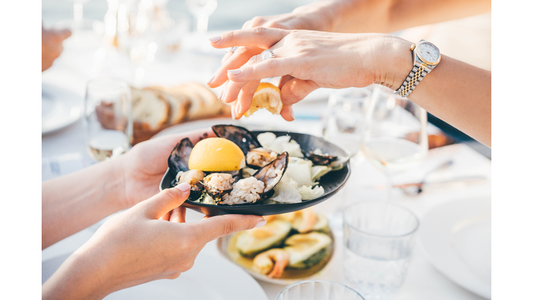 Close up of a woman's hand squeezing lemon juice on to mussels, enjoying meal in a restaurant.