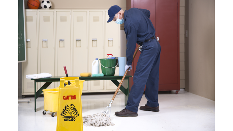 Senior Adult Janitor mops floor in school locker room.