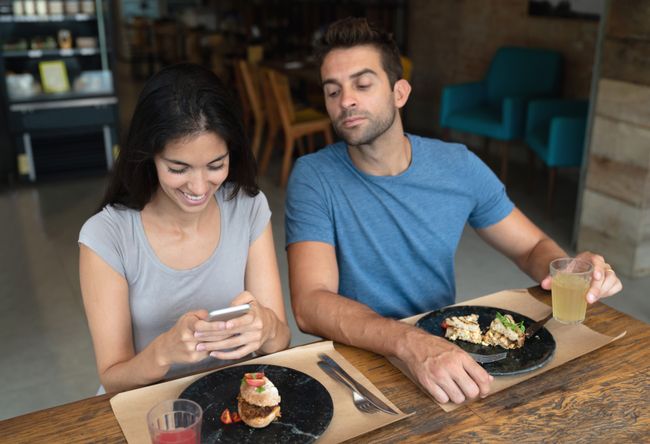 Woman texting at a restaurant and boyfriend trying to see her phone