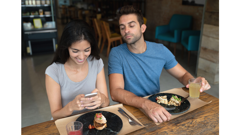 Woman texting at a restaurant and boyfriend trying to see her phone