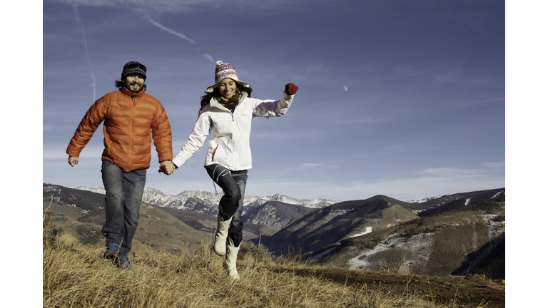 Couple holding hands and running in the mountains.