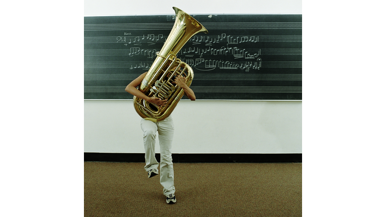 Young woman struggling to hold tuba in front of music on blackboard
